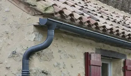 Gouttière et descente d'eaux pluviales posées sur une façade en pierre